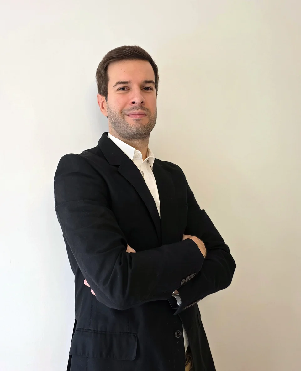 David Fernandes, o fundador do Sharpyield, de casaco escuro e camisa branca, com os braços cruzados, em frente a uma parede clara